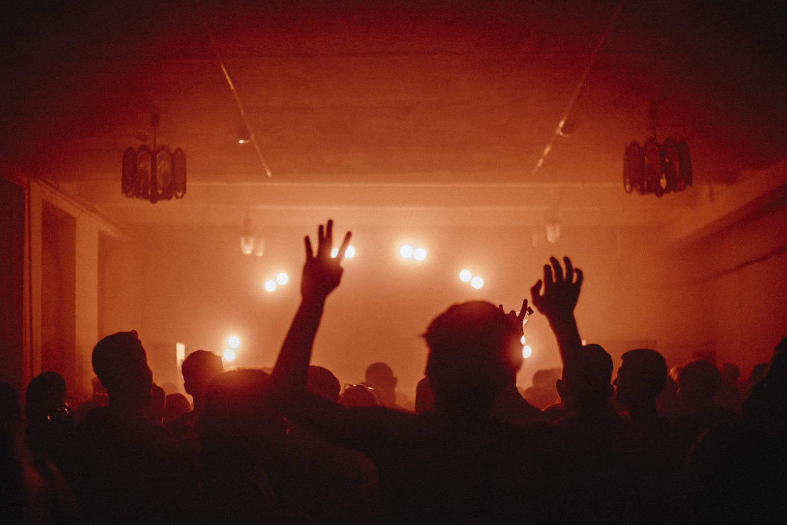 Silhouetted people in a warm, dimly lit room with their hands in the air