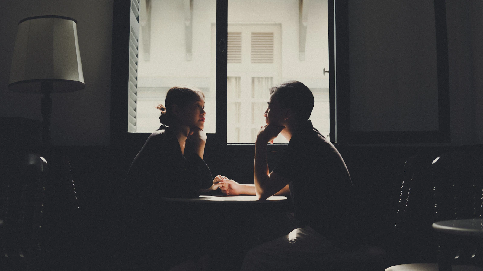 Two people leaning in across a small table in low light, deep in conversation