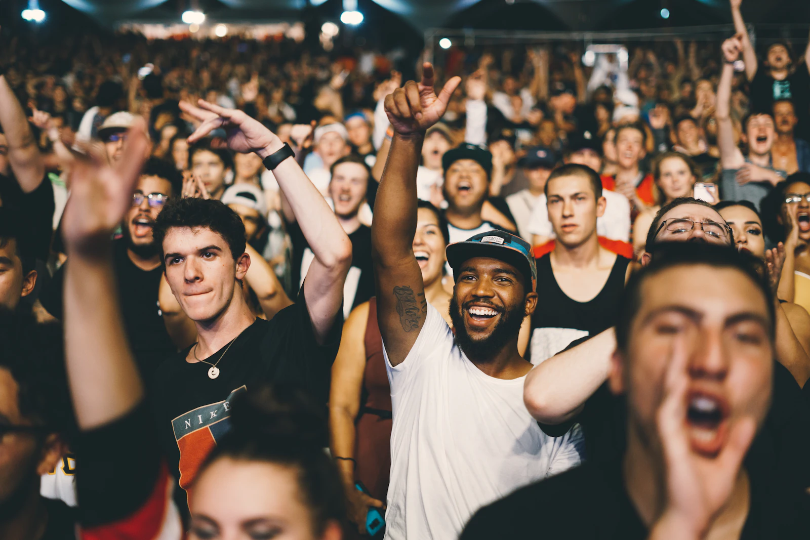 A packed crowd at a live event, arms raised and faces lit up