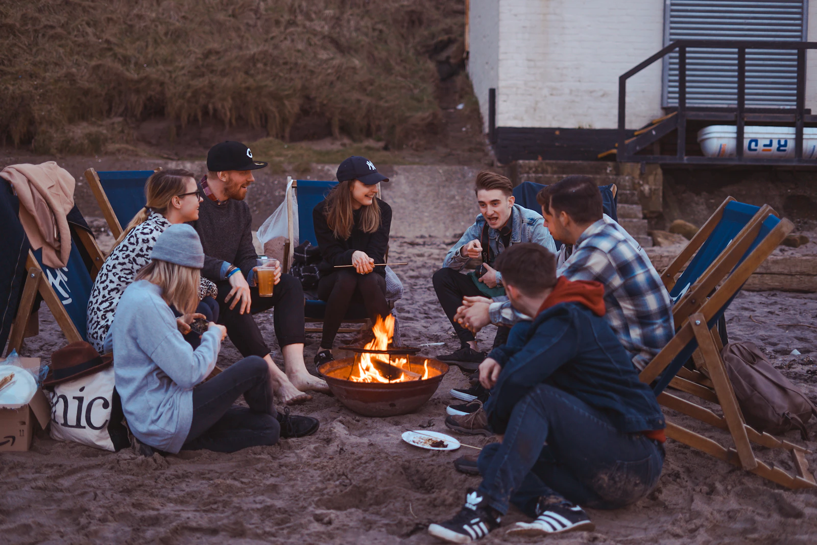 Friends gathered in a circle around a fire at dusk, talking